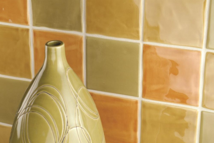 Keramikfliesen in warmen Braun- und Orangetönen mit dekorativer Vase im Vordergrund Nahaufnahme von glänzenden, quadratischen Wandfliesen in Braun- und Orangetönen, vor denen eine verzierte Keramikvase steht