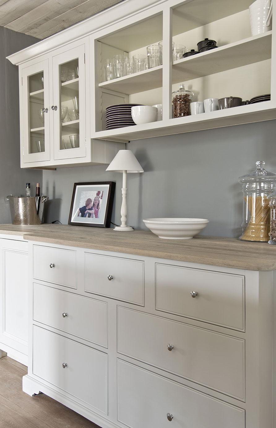 Moderne Landhaus-Küchenzeile aus Holz mit weißen Schränken, Schubladen und offenen Regalen Weiße Küchenzeile im Landhausstil mit Holzarbeitsplatte, Schubladen, Glastüren, offenen Regalen, Geschirr und dekorativen Elementen