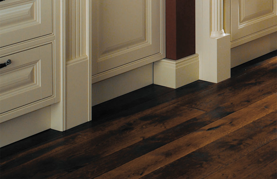 Sockelleiste für Küchenmöbel in klassischem Design mit Holzfußboden Detailansicht einer hellen Sockelleiste an Küchenmöbeln vor einem dunklen Holzfußboden