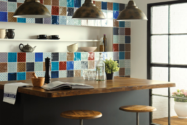 Moderne Küche mit Holztheke, bunten Fliesen und zwei Barhockern im Industrial-Design Stylische Küche mit Holztheke, bunten Wandfliesen, Regal mit Geschirr und Barhockern im Industriestil