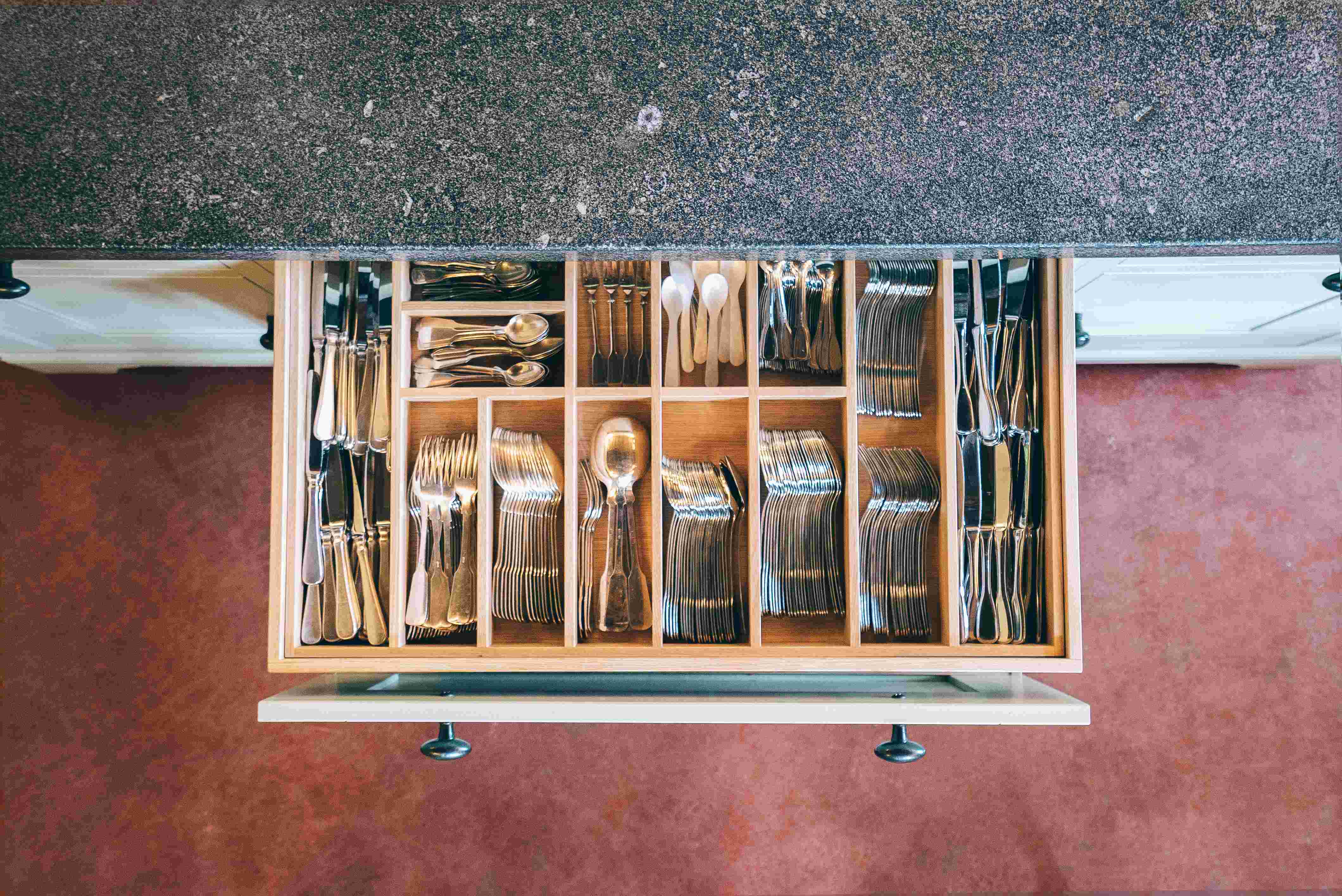 Geöffnete Küchenschublade mit sortiertem Besteck, darunter Gabeln, Messer, Löffel und Teelöffel aus Edelstahl, ordentlich in einem Holzeinsatz angeordnet