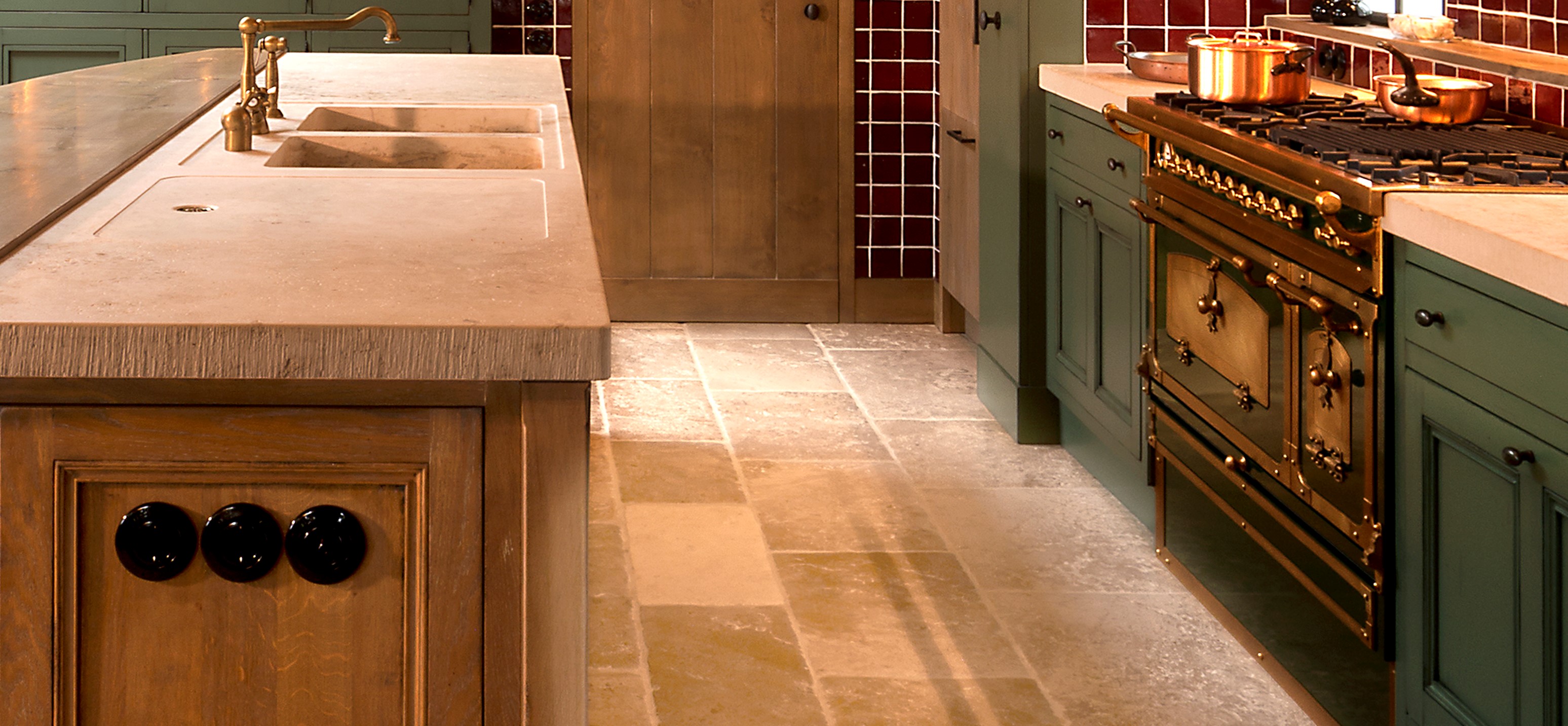 Hochwertige Landhausküche mit Naturstein-Arbeitsplatten und Vintage-Gasherd Detailansicht einer eleganten Landhausküche mit Naturstein-Arbeitsplatte, goldfarbenem Gasherd, Spülbecken und grün lackierten Holzfronten