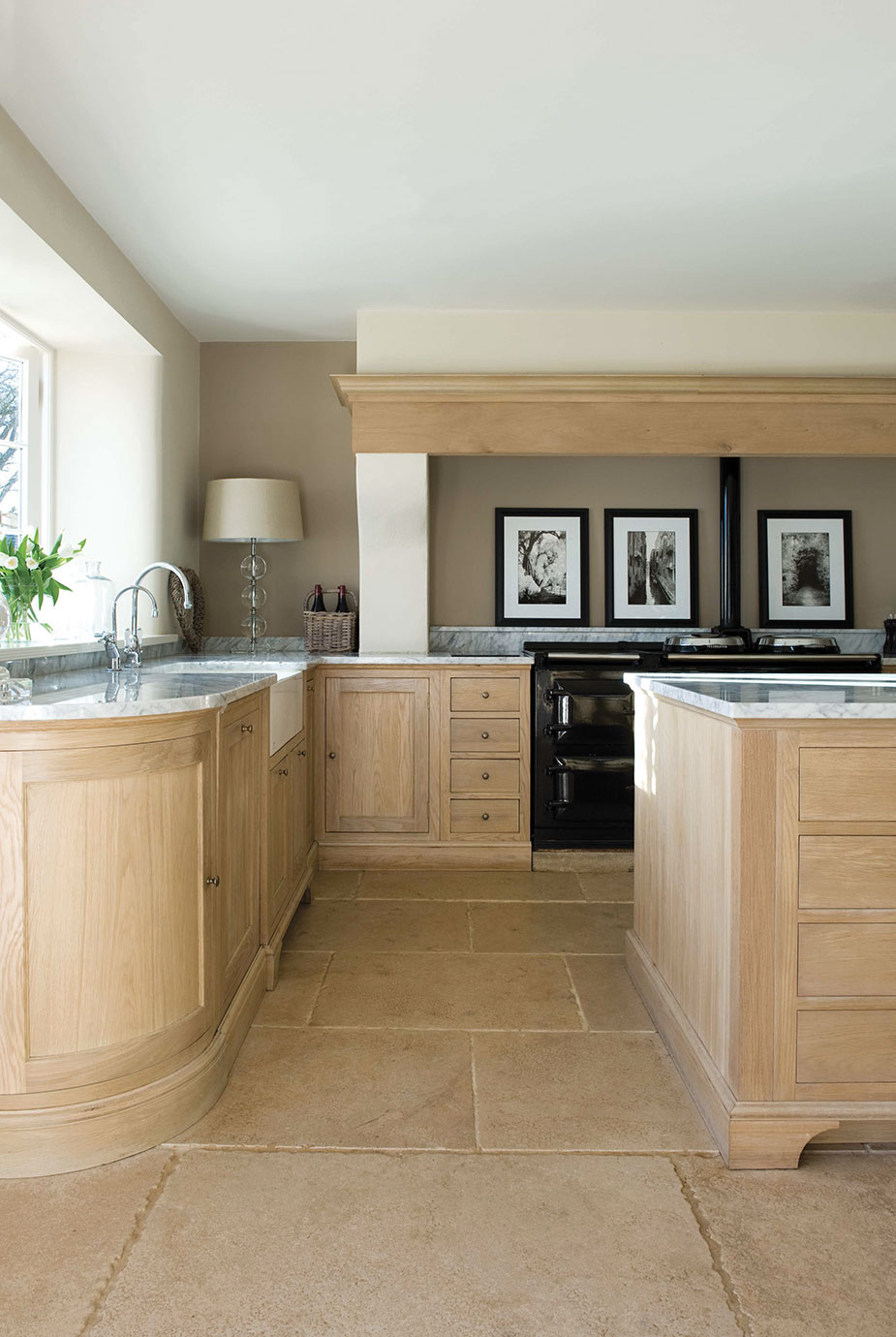 Moderne Landhausküche mit hellen Holzmöbeln und Arbeitsplatten aus Marmor Helle Landhausküche mit naturfarbenen Holzmöbeln, Arbeitsplatten aus Marmor, großem Fenster und stilvoller Dekoration