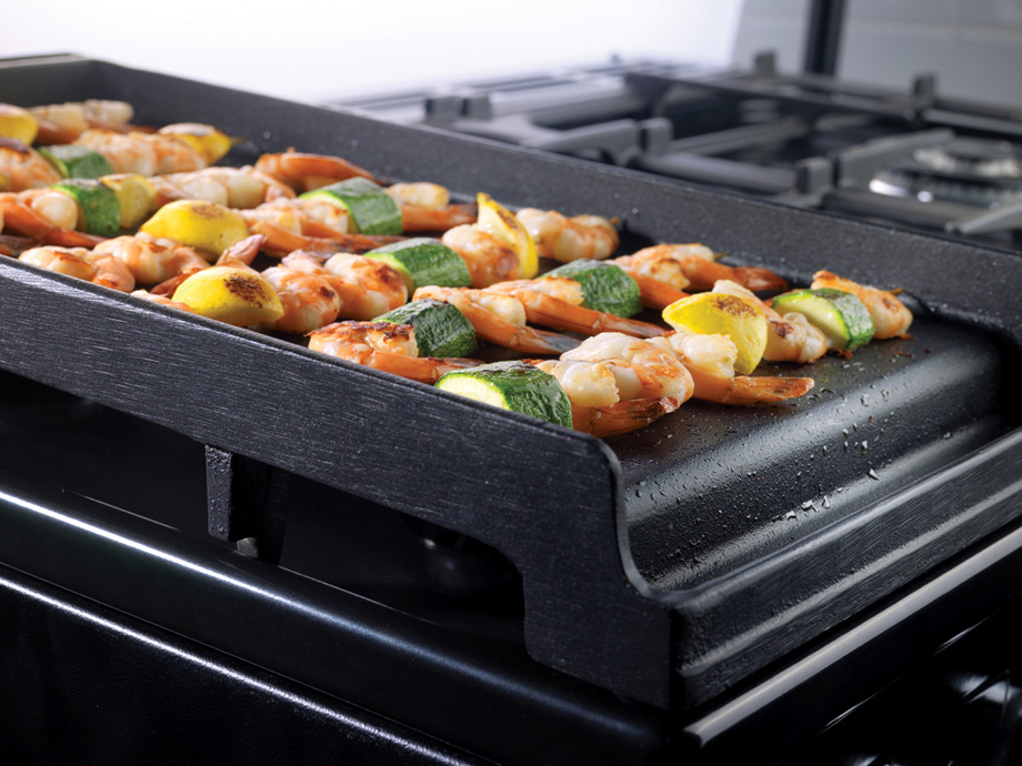 Grillplatte mit Garnelen-Spießen, Zucchini und Zitrone auf einem Gasherd – ideal für gesundes Grillen zuhause Frische Garnelen-Spieße mit Zucchini und Zitronenstücken werden auf einer gusseisernen Grillplatte auf einem Gasherd gegrillt