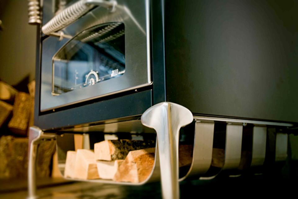 Moderner Kaminofen aus Edelstahl mit Holzlagerfach – stilvolles und praktisches Heizgerät für Ihr Zuhause Nahaufnahme eines modernen Kaminofens aus Edelstahl mit Holzlagerfach darunter, darin gestapeltes Kaminholz