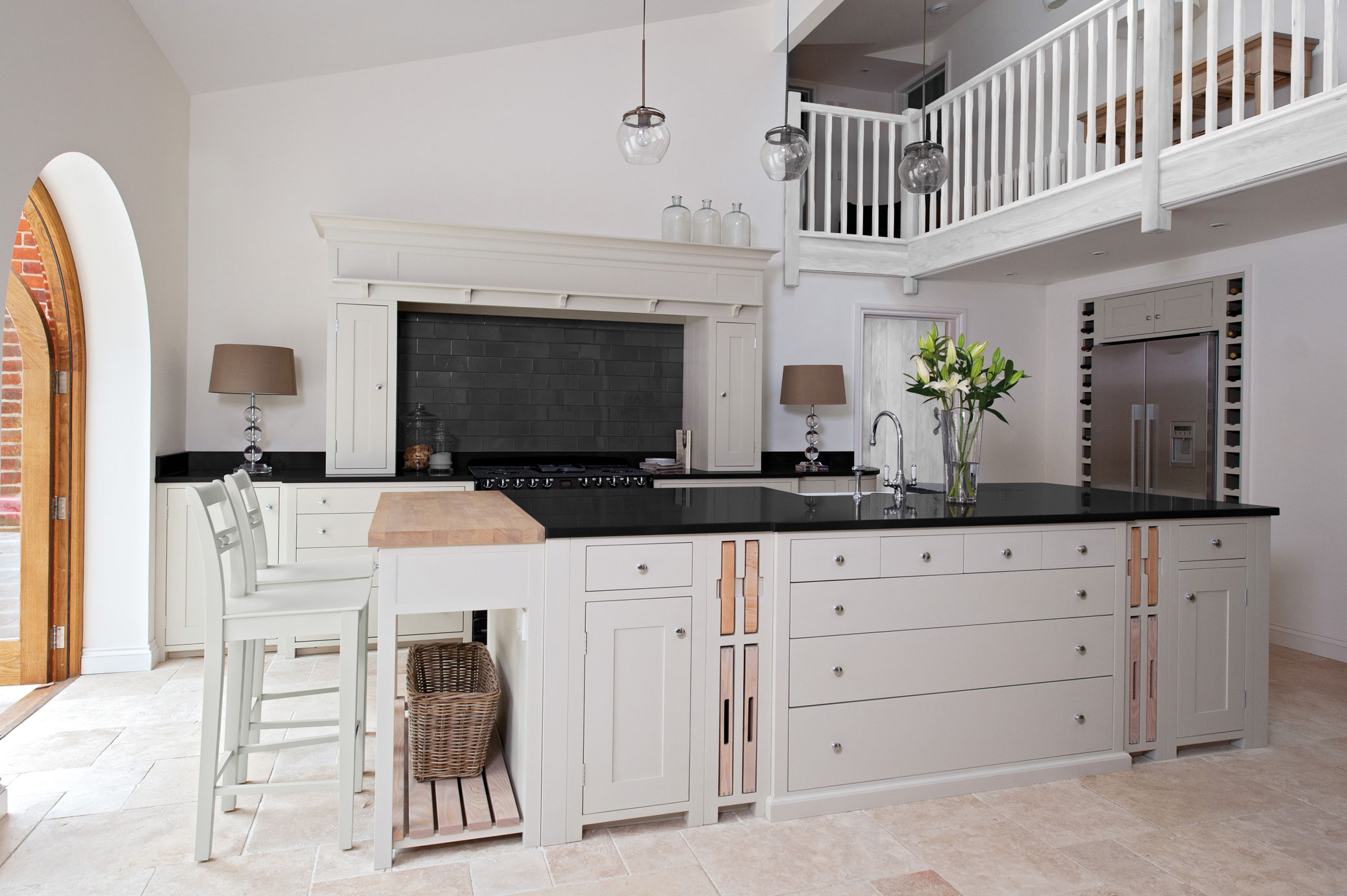 Moderne Landhausküche mit Kücheninsel, hellen Fronten, schwarzer Arbeitsplatte und komfortabler Sitzgelegenheit Große, helle Landhausküche mit Kochinsel, schwarzen Arbeitsflächen, Barhockern, hochwertigen Geräten und eleganter Dekoration
