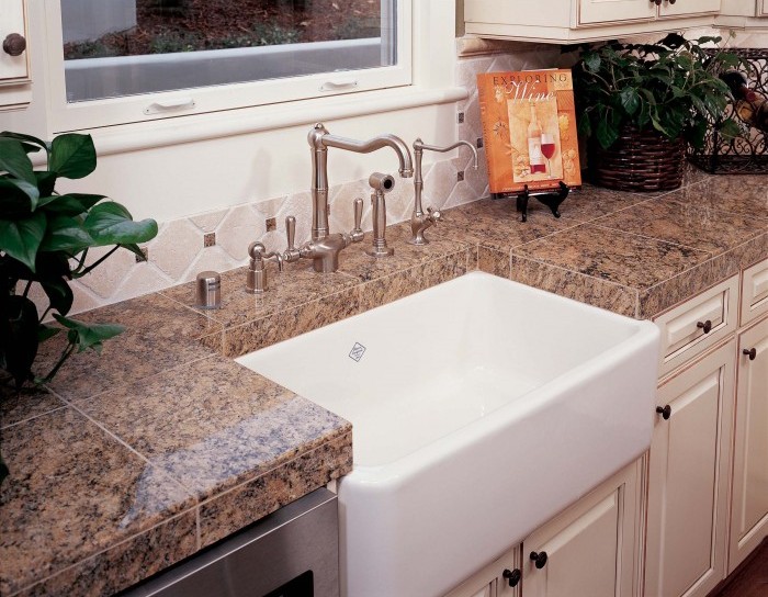 Küchenspüle im Landhausstil mit Granit-Arbeitsplatte und Edelstahlarmatur Große weiße Landhausstil-Küchenspüle mit moderner Edelstahlarmatur und brauner Granit-Arbeitsplatte in einer hellen Küche