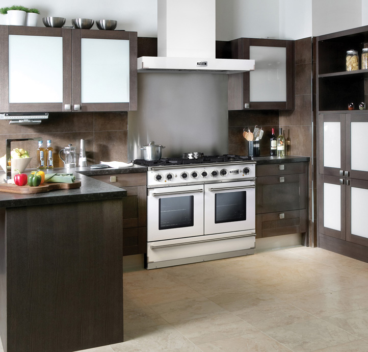 Moderne Einbauküche mit dunklen Schränken und großem Gasherd Hochwertige moderne Küche mit dunklen Holzschränken, Gasherd, Dunstabzugshaube und Kücheninsel, auf der frisches Gemüse liegt.