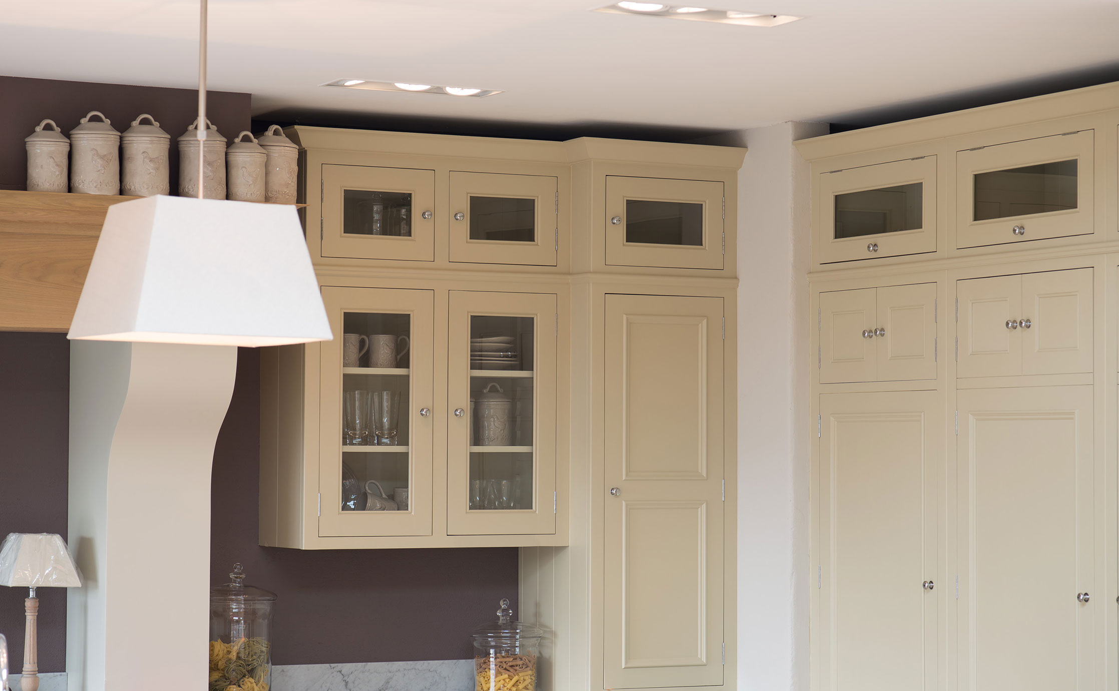 Küchenschränke im Landhausstil aus Holz mit Glasfronten in cremefarbener Optik Küchenschränke im Landhausstil aus cremefarbenem Holz, teilweise mit Glastüren, dekoriert mit Keramikdosen und Gläsern