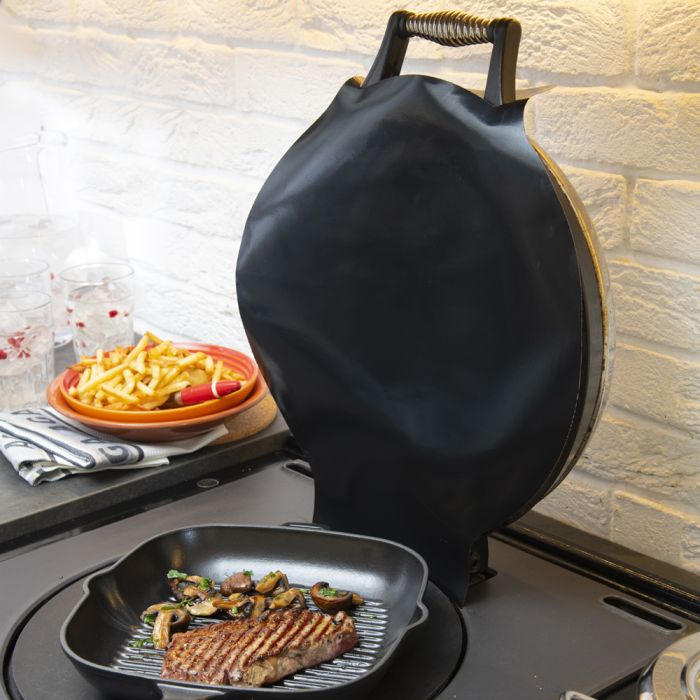 Grillpfanne mit gegrilltem Steak und Pilzen, im Hintergrund Teller mit Pommes und Gläser auf Küchentheke