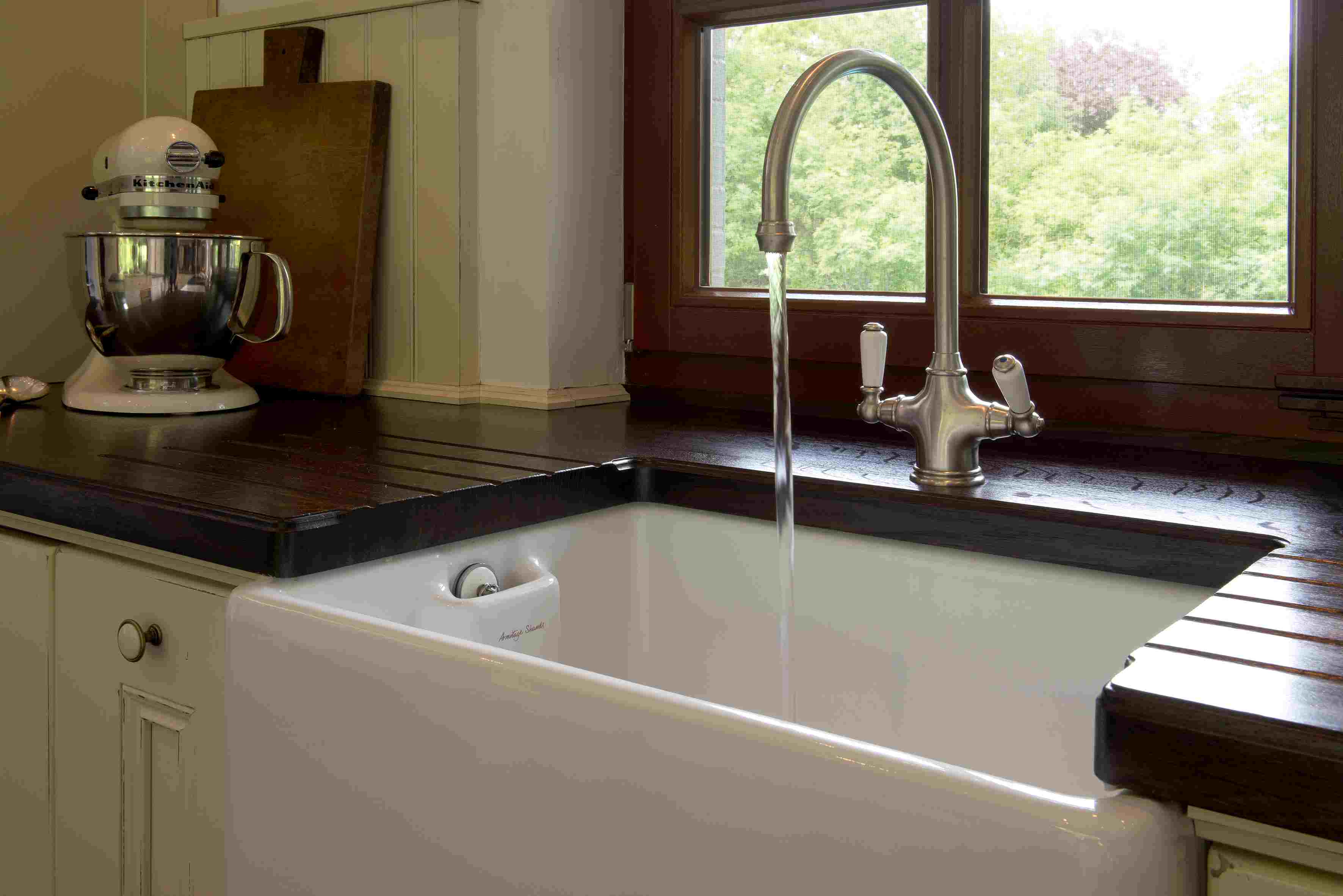 Küchenspüle im Landhausstil mit laufendem Wasserhahn, Holztischplatte und Küchenmaschine neben dem Fenster