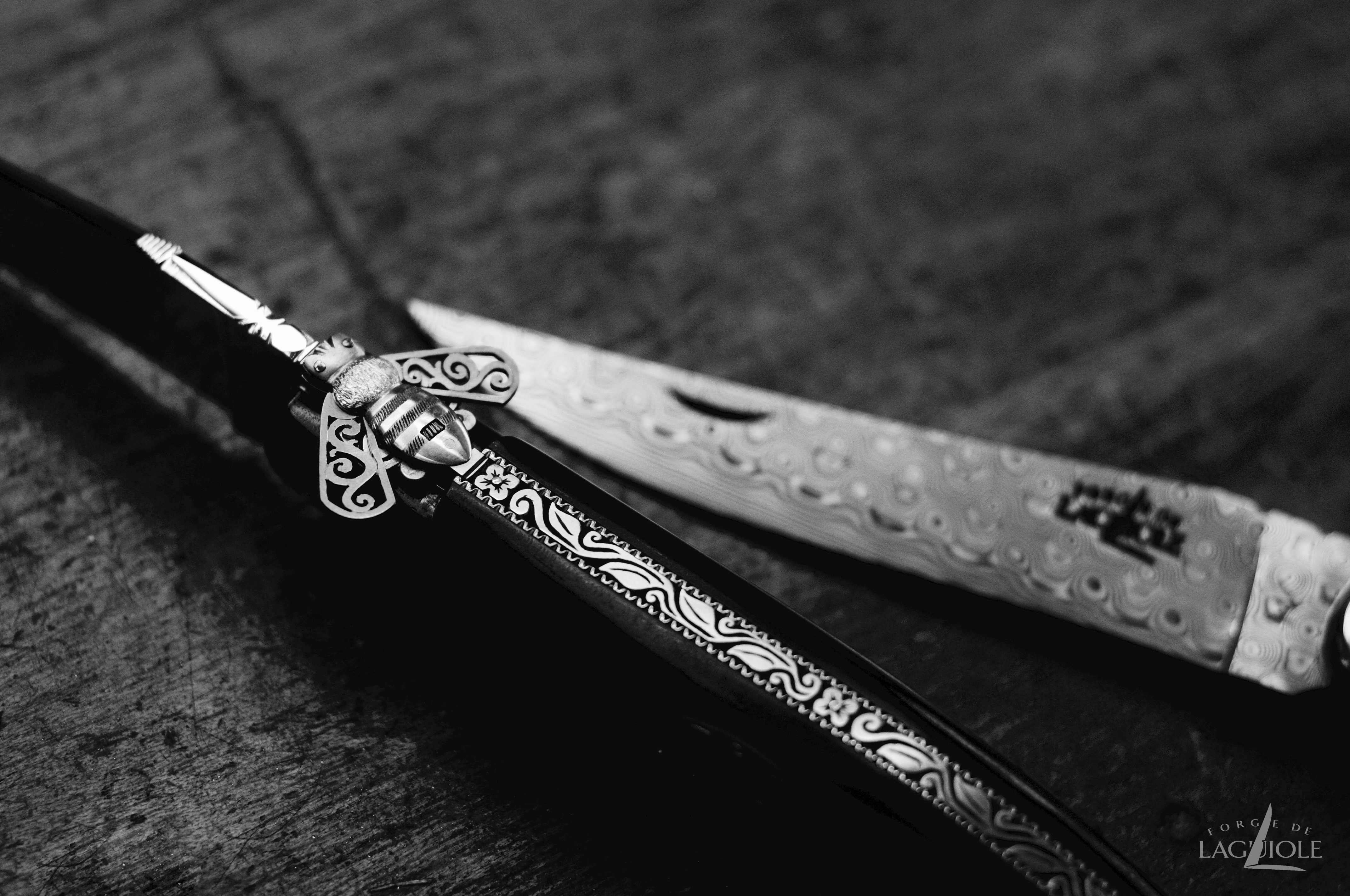 Laguiole Damastmesser mit detailreicher Gravur und Biene, handgefertigt Nahaufnahme eines handgefertigten Laguiole Messers aus Damaststahl mit kunstvoller Verzierung und charakteristischer Biene auf dem Griff