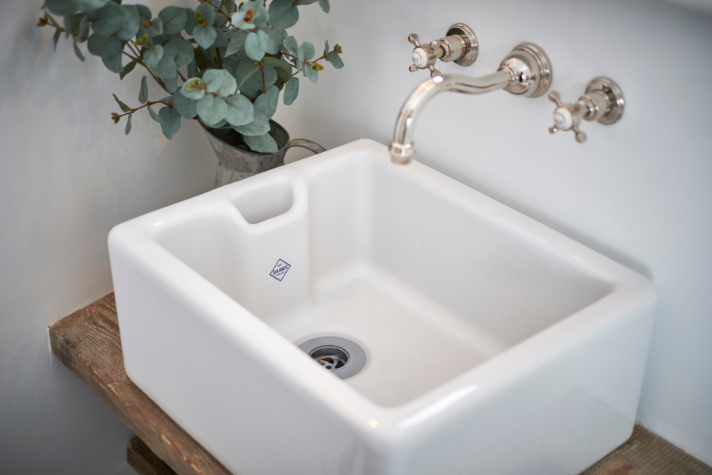 Keramik Waschbecken im Landhausstil mit Wandarmatur und Holzablage – charmantes Badezimmerelement Rechteckiges weißes Keramik Waschbecken mit Wandarmatur, auf Holzablage, und Dekorvase mit Eukalyptus-Zweigen