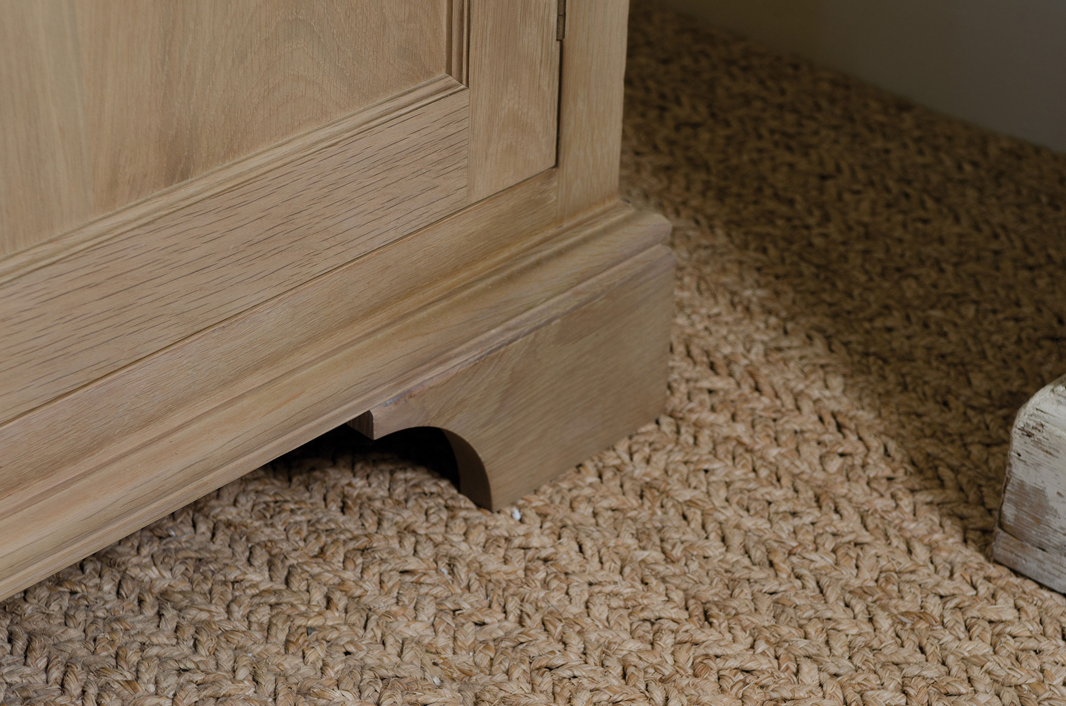Detailansicht Sockel eines Massivholzschranks auf geflochtenem Teppich Nahaufnahme des Sockels eines Schranks aus hellem Holz auf einem grob geflochtenen Teppichboden