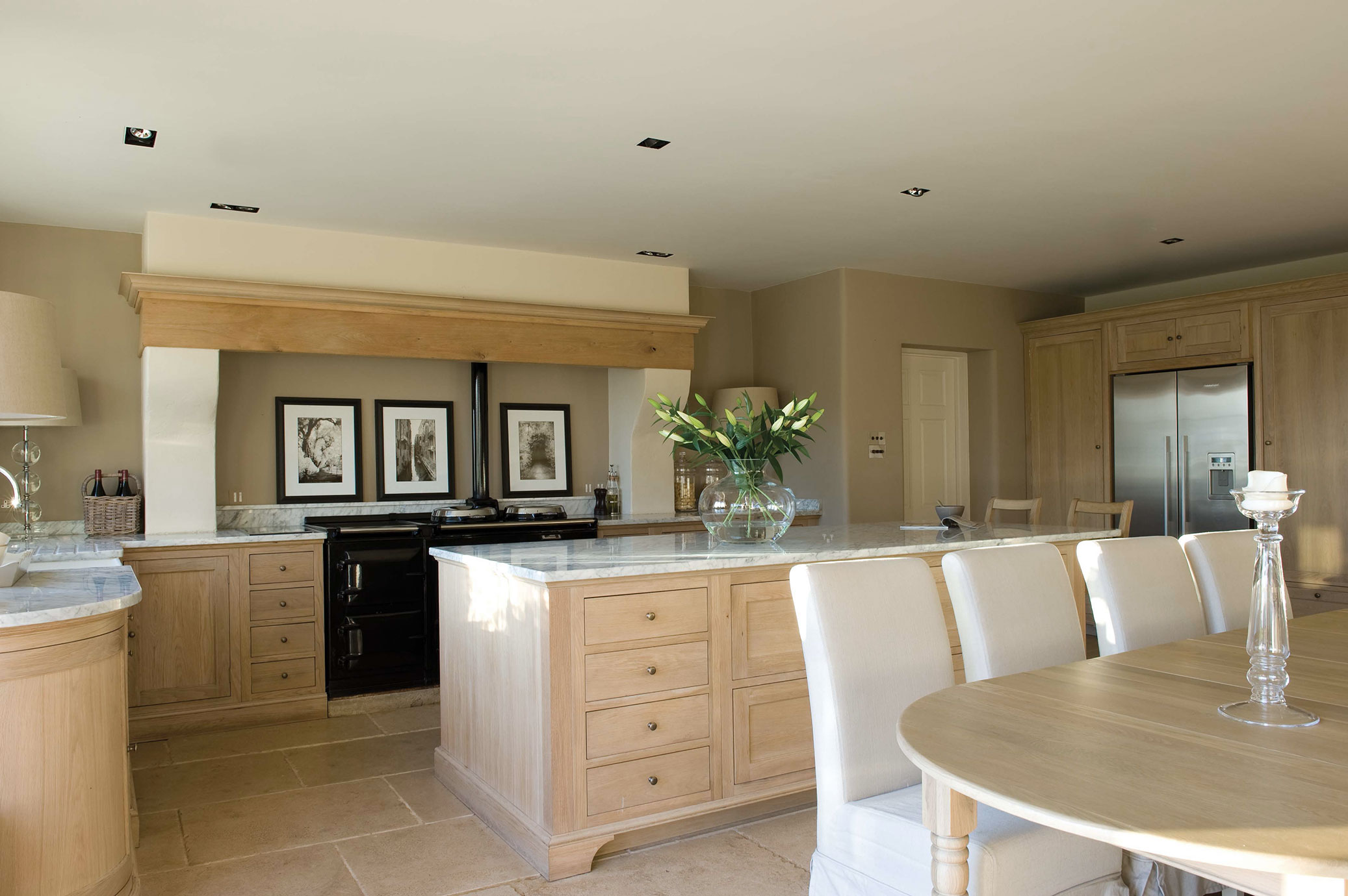 Moderne Landhausküche mit Kücheninsel, Holzfronten und Marmordetails Helle Einbauküche im Landhausstil mit großer Kücheninsel, Holzschränken, Marmorarbeitsplatten und Esstisch mit weißen Stühlen