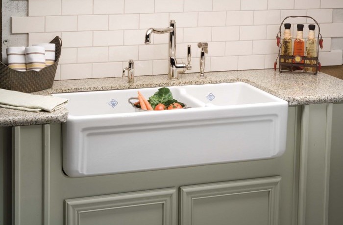 Landhausstil-Küchenspüle aus Keramik mit Gemüse und moderner Armatur auf Granitarbeitsplatte Weiße Keramikspüle im Landhausstil mit frischem Gemüse, Metallarmatur und Granitarbeitsplatte in einer Küche