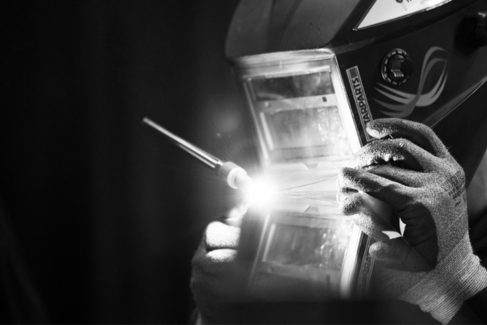 Schweißer bei der Arbeit mit Schutzhelm und Handschuhen Person mit Schweißhelm und Schutzhandschuhen führt eine Schweißarbeit aus, heller Lichtbogen sichtbar