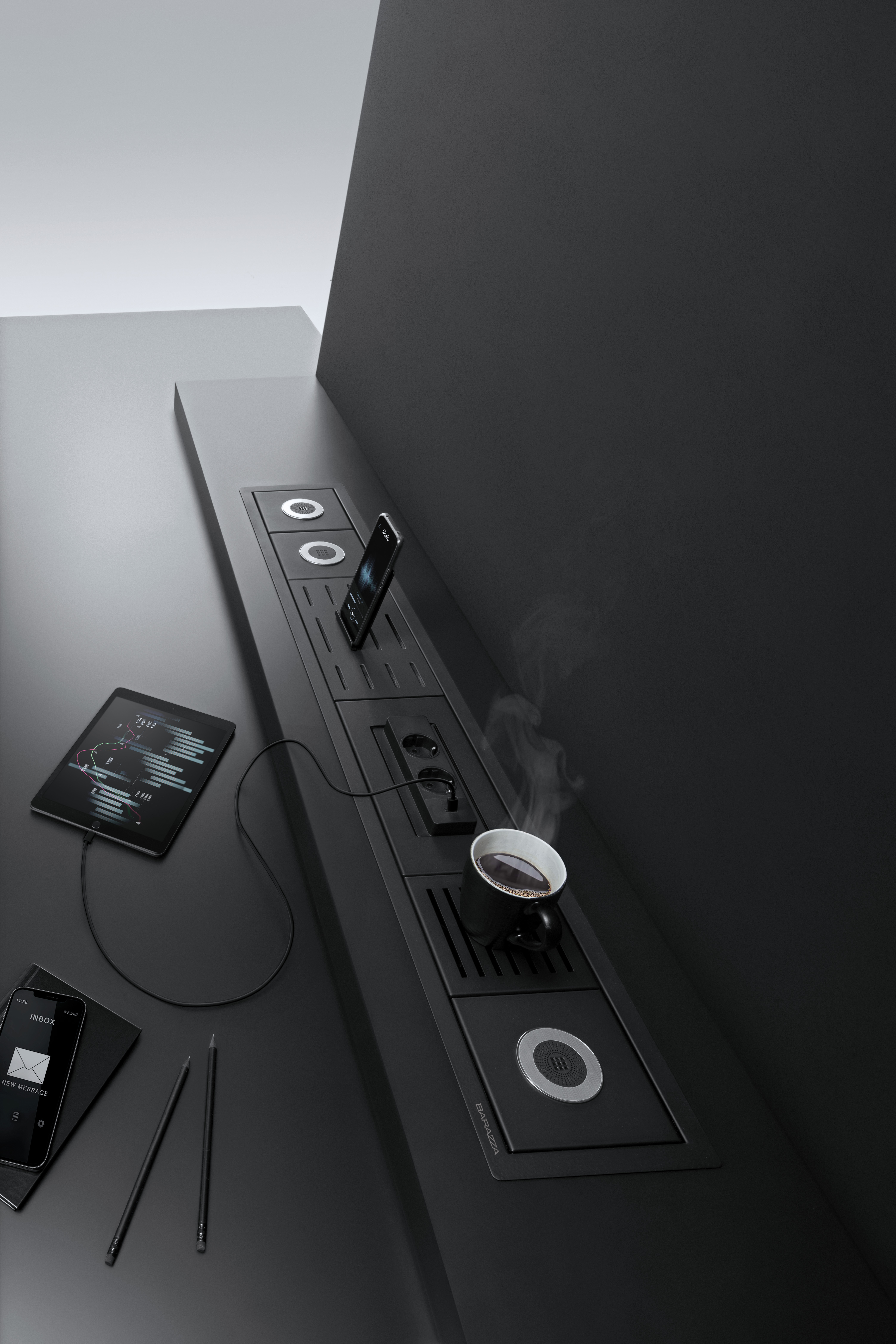 Innovatives Küchensystem mit integriertem Induktionsherd, Steckdosen und Ablage für Smartphone sowie Tablet Modernes Küchensystem mit integriertem Induktionskochfeld, Steckdosen, einer Tasse Kaffee, Smartphone und Tablet auf dunkelgrauer Arbeitsfläche