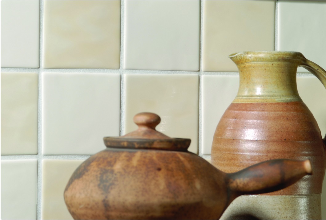 Matte, quadratische Wandfliesen in Beige mit einem handgefertigten Keramiktopf und einem Krug im Vordergrund, Küchenambiente