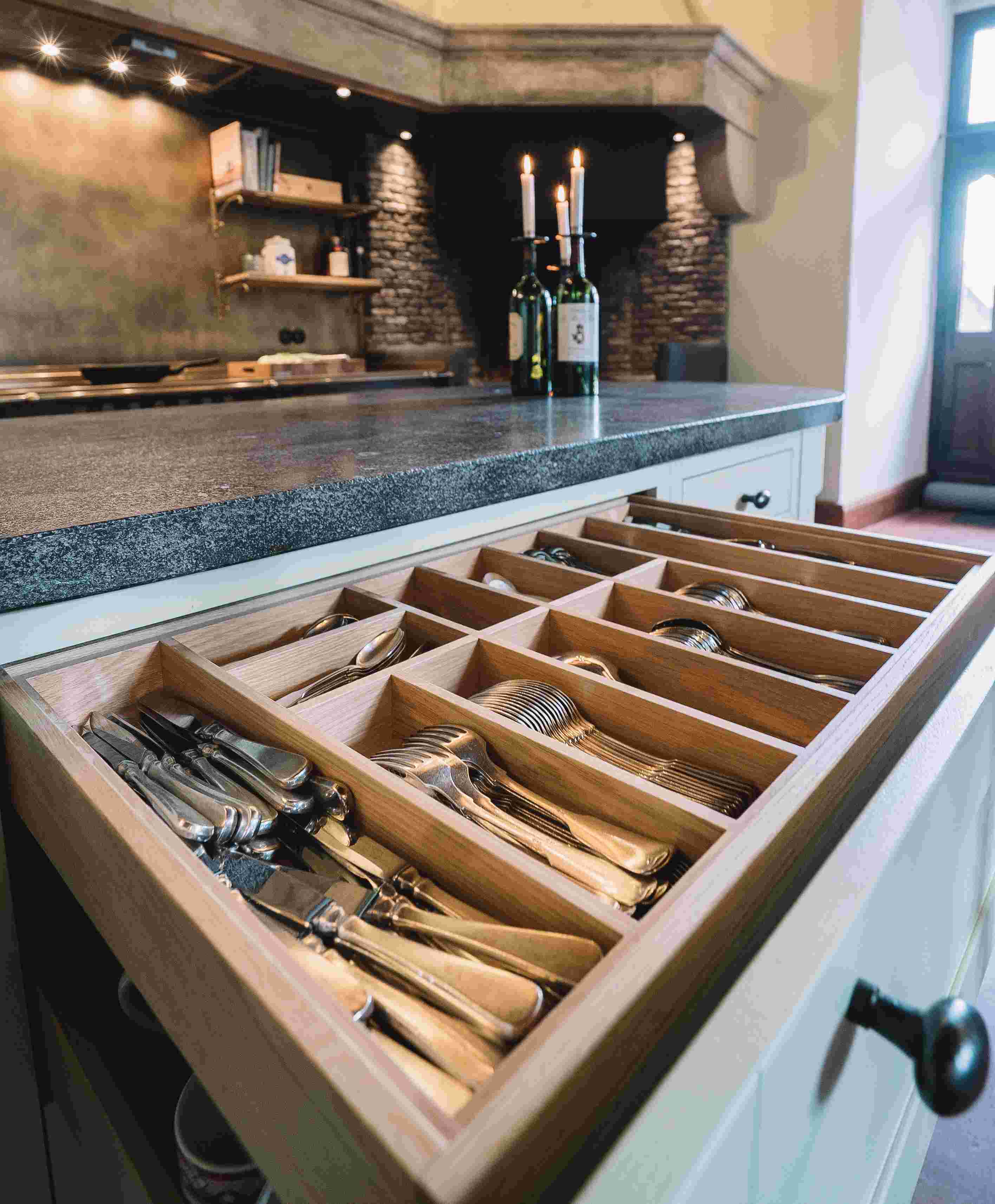 Detailaufnahme einer geöffneten Schublade mit stilechtem Holzbesteckeinsatz, gefüllt mit Besteck in einer modernen Küche mit dunkler Arbeitsplatte und Dekoration