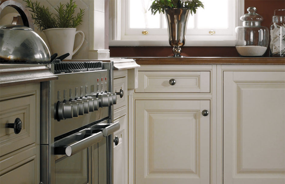 Hochwertige Landhausküche mit cremefarbenen Schränken und moderner Edelstahlkochstelle Detailaufnahme einer eleganten Landhausküche mit cremefarbenen Küchenfronten, Edelstahlherd, Teekanne und Dekoration auf der Arbeitsplatte