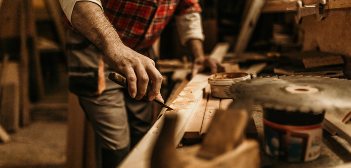 Handwerker bearbeitet Holz in einer Werkstatt mit verschiedenen Werkzeugen Hand eines Mannes in kariertem Hemd, der in einer Werkstatt ein Stück Holz mit einem Hobel bearbeitet, im Vordergrund verschiedene Werkzeuge