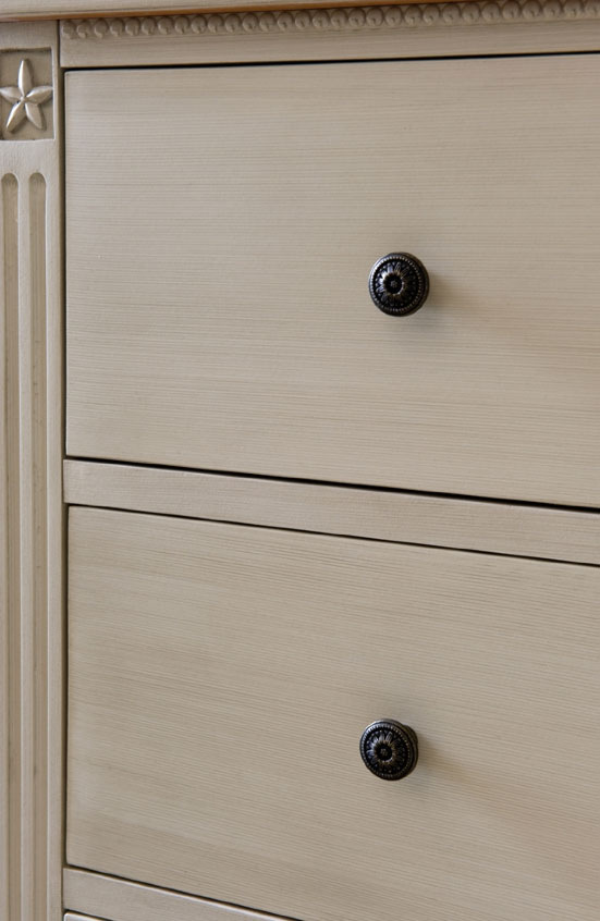 Detailansicht einer cremefarbenen Kommode mit zwei Schubladen und dekorativen Griffen Nahaufnahme einer klassischen Kommode in Creme mit zwei Schubladen und runden Metallgriffen