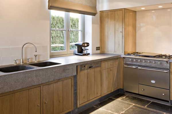 Moderne Küche mit Holzfronten, grauer Steinarbeitsplatte, Gasherd und Doppelspüle Helle Einbauküche mit Holzschränken, Steinarbeitsplatte, großem Gasherd, Doppelspüle und Kaffeemaschine am Fenster