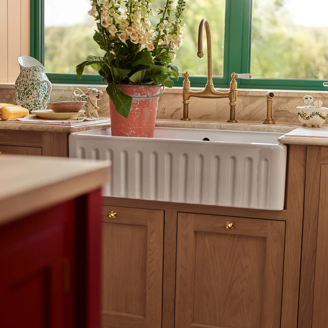Weiße Keramik-Butler-Spüle mit geriffelter Front in Eichen-Unterschrank, kombiniert mit Messing-Brückenarmatur; dekorative Arbeitsfläche mit Blumentopf – Produktfoto einer hochwertigen Landhaus-Küchenspüle