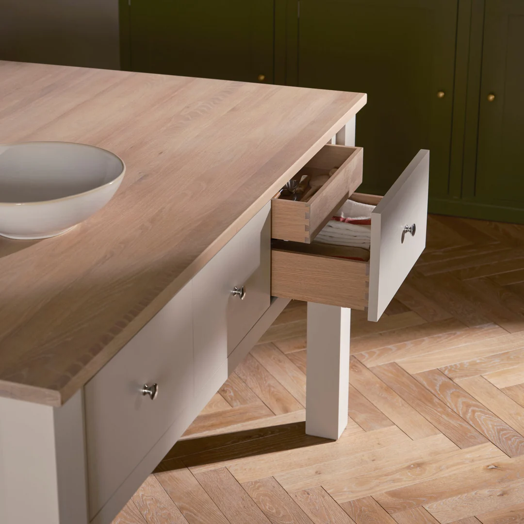 Detailansicht einer cremefarbenen Kücheninsel mit massiver Eichenarbeitsplatte; geöffnete Besteckschublade mit Dovetail-Zinken, Knopfgriffen und stabilen Beinen – ideale Arbeits- und Stauraumlösung