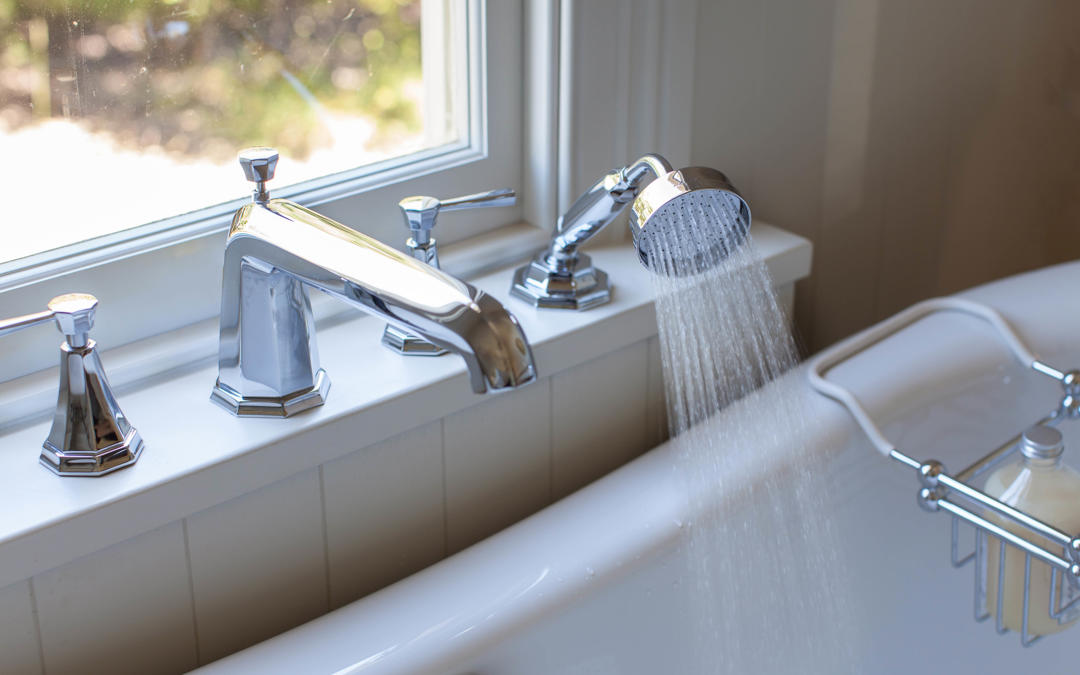 Glänzende Badewannenarmatur aus Chrom mit separater Handbrause, fließendem Wasserstrahl und Wannenrandmontage vor Fenster – hochwertiges Set für die Badewanne