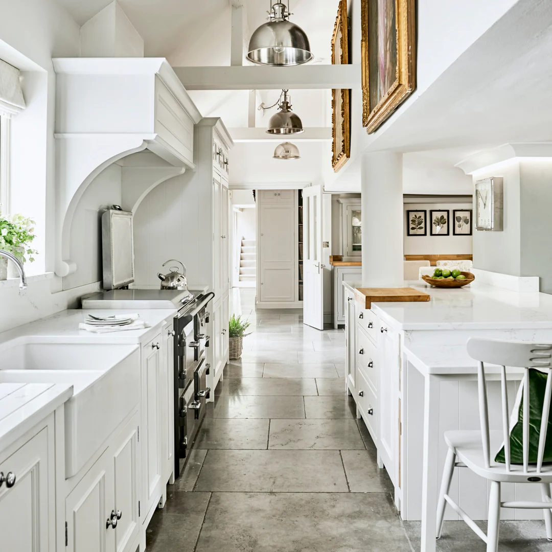 Elegante weiße Landhausküche mit Shaker-Schränken, Keramik-Doppelspüle, schwarzem Range Cooker, Marmoroptik-Arbeitsplatten, Kücheninsel und Pendelleuchten – ideale Produktdarstellung für Einbauküche