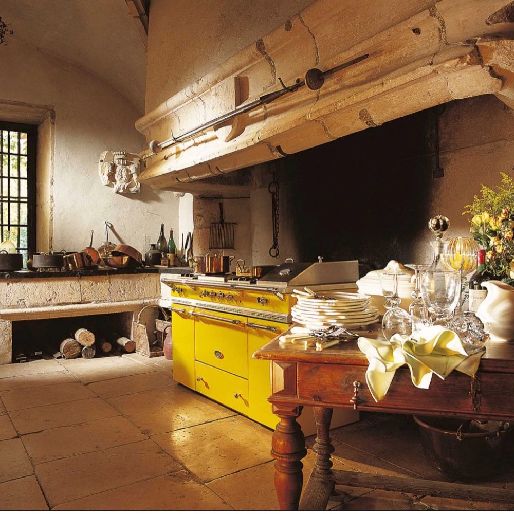 Rustikale Landhausküche mit leuchtend gelbem Standherd/Backofen; hochwertiger Profi-Herd als Blickfang neben Holztisch mit Geschirr – ideal für traditionelles Kochen und stilvolle Kücheneinrichtung