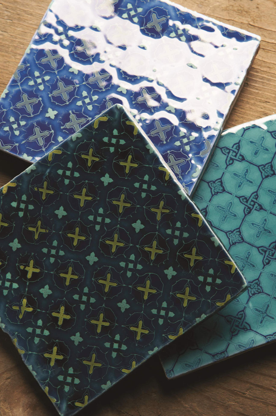 Handgefertigte Keramikfliesen mit orientalischem Muster in Blau- und Türkistönen Drei quadratische, handgemachte Keramikfliesen mit verschiedenfarbigen, orientalischen Mustern liegen auf einer Holzoberfläche