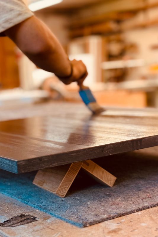 Hand trägt mit Pinsel Möbellack auf eine Holzplatte in der Werkstatt auf – gleichmäßiges Finish für Möbel, Schutz vor Kratzern und Feuchtigkeit