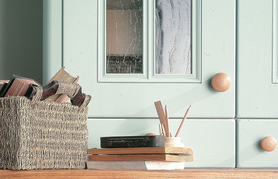Dekorative Aufbewahrung: Geflochtener Korb mit Büchern, Holzstiftehalter und Bücher vor mintgrünem Schrank Geflochtener Korb mit alten Büchern, Holzstiftehalter und Bücherstapel auf Holzoberfläche vor mintgrünem Schrank mit Glastüren