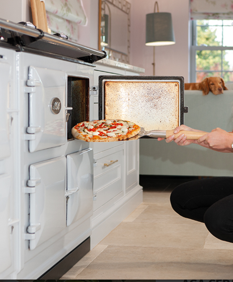Hand schiebt mit einer Pizzaschaufel mit Holzgriff eine frisch belegte Pizza in einen weißen Küchenofen