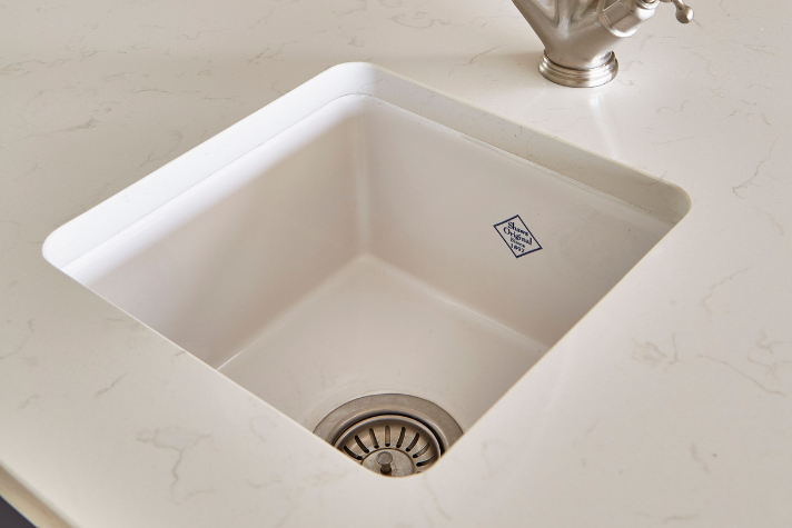 Quadratisches Spülbecken aus weißem Keramik in moderner Küchenarbeitsplatte Nahaufnahme eines quadratischen weißen Spülbeckens mit Abfluss und Wasserhahn in einer hellen Küchenarbeitsplatte