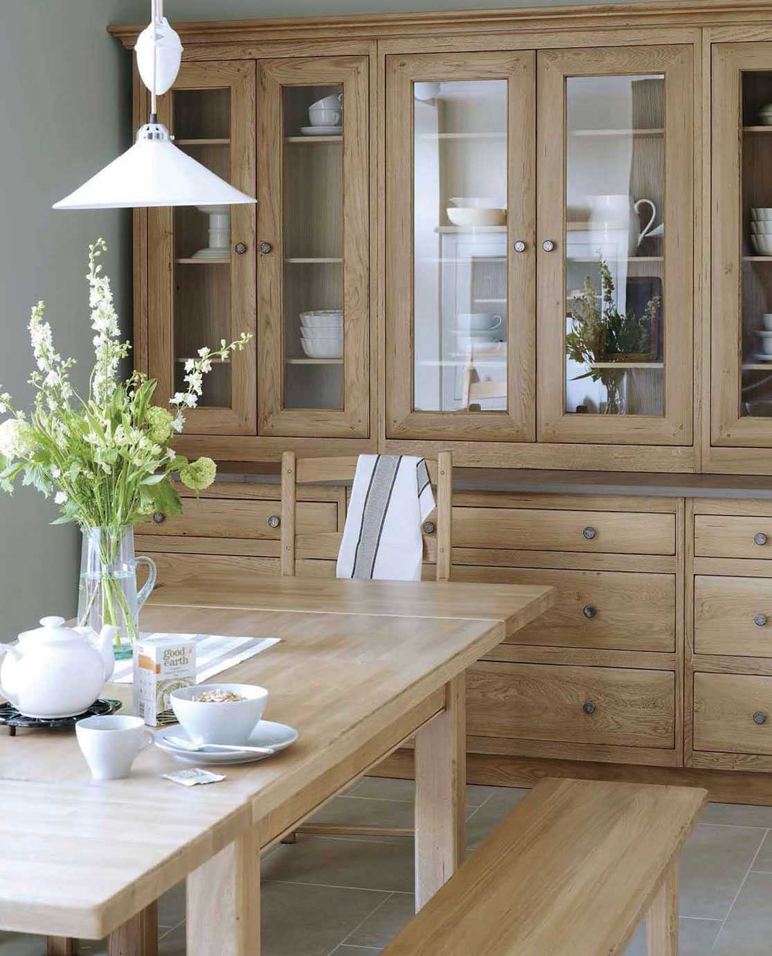 Esszimmer im Landhausstil mit massivem Holztisch, Vitrine und liebevoll gedecktem Frühstückstisch Helles Esszimmer mit Holztisch, Bank, Stuhl, Glasvitrine, Porzellangeschirr und frischen Blumen in Vase auf dem Tisch