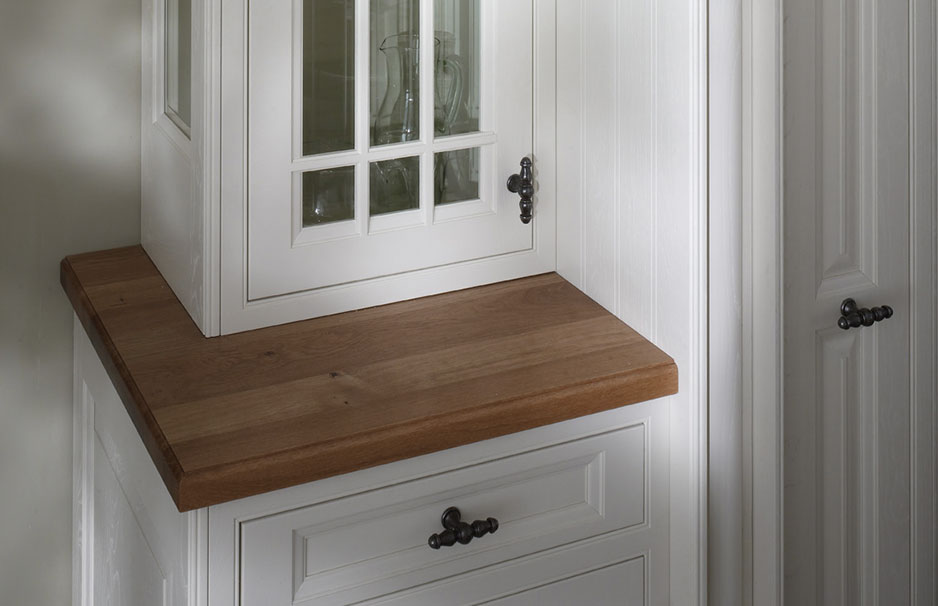 Ecke einer weißen Landhausküche mit Holzarbeitsplatte und Vitrinenschrank Detailaufnahme einer weißen Landhausküche mit massivem Holzboden, Vitrinenschrank mit Glastüren und dekorativen Metallgriffen