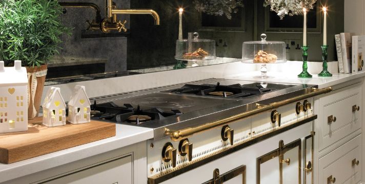 Eleganter weißer Range Cooker mit 4-flammigem Gaskochfeld, Messingknebeln und Reling, eingebaut in eine klassische Küche mit heller Arbeitsplatte; stilvolle Deko und Glasglocken im Hintergrund
