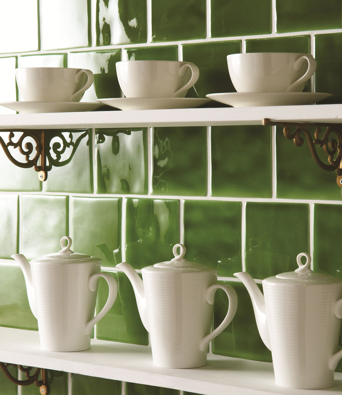 Elegantes Teeservice aus weißem Porzellan vor grünen Fliesen auf Küchenregal Weißes Porzellan-Teeservice mit Tassen und Teekannen auf weißen Regalen vor glänzenden grünen Fliesen