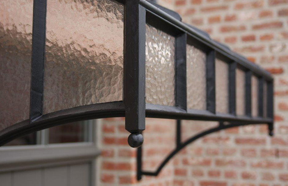 Vordach aus Schmiedeeisen mit getöntem Glas für Eingangsbereich Detailaufnahme eines dekorativen Vordachs aus Schmiedeeisen mit getöntem Glas vor einer Backsteinfassade