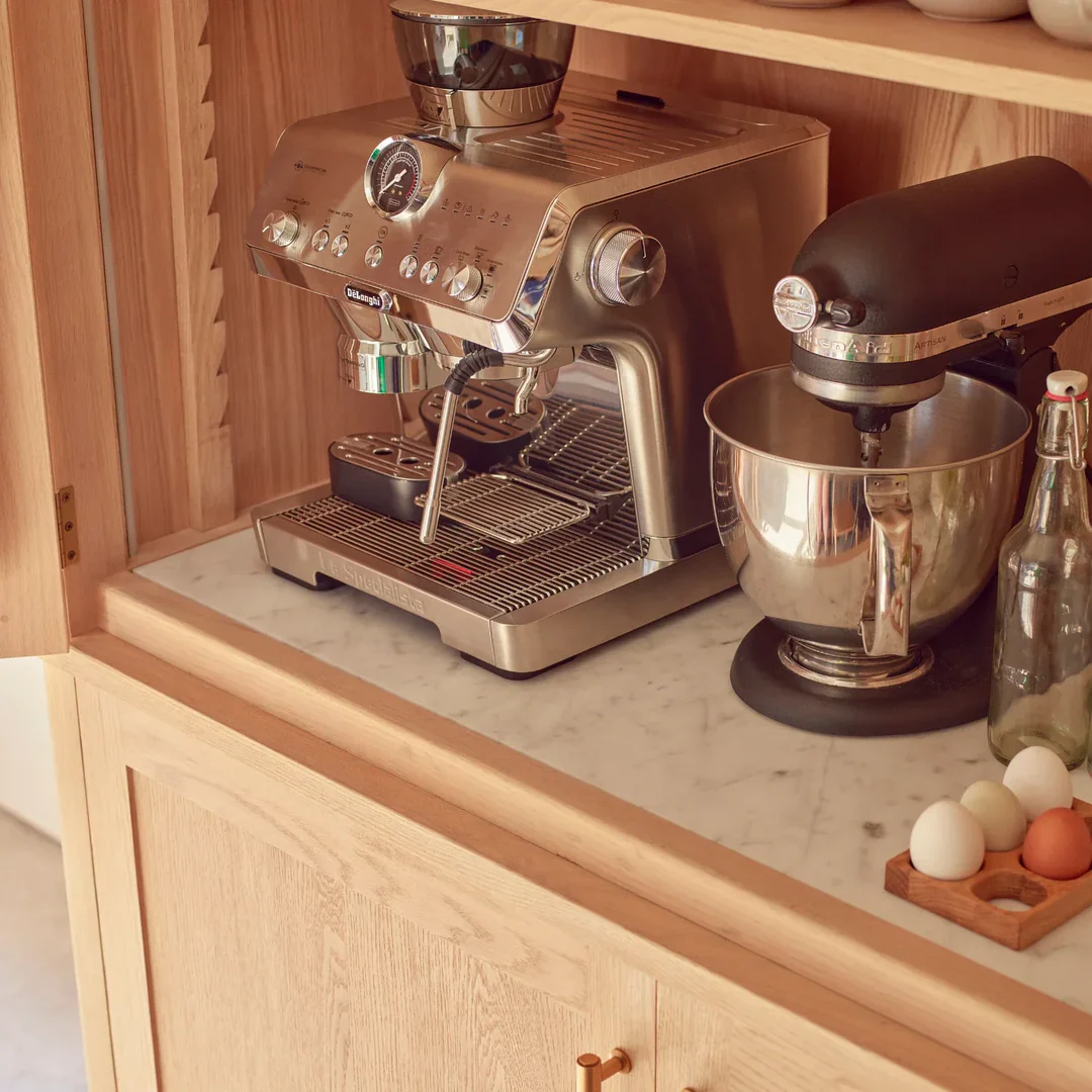 Hochwertige Siebträger-Espressomaschine aus Edelstahl neben Küchenmaschine auf Marmorarbeitsplatte in Holzschrank; Dampfdüse, Manometer und Abtropfblech sichtbar – ideal für Barista-Genuss zu Hause