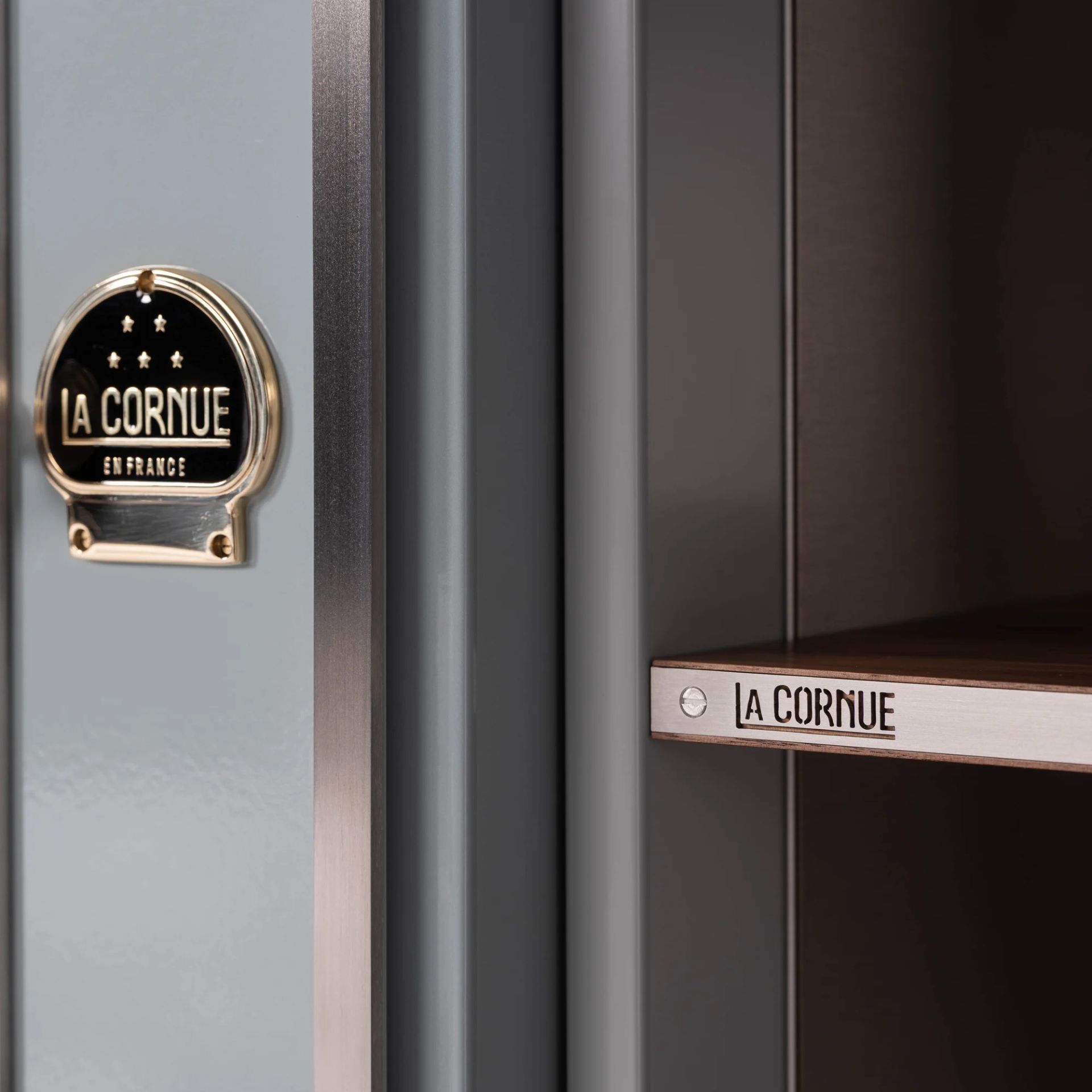 Detailaufnahme des La-Cornue-Emblems und der Edelstahlablage eines grauen Premium-Standherds; elegante Verarbeitung für die hochwertige Küche