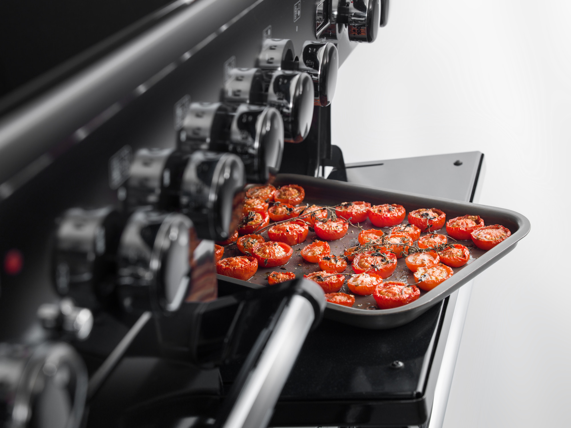 Backblech mit gewürzten und gerösteten Tomaten in einem modernen Backofen Nahaufnahme von halbierten, mit Kräutern gewürzten Tomaten auf einem Backblech in einem modernen Ofen