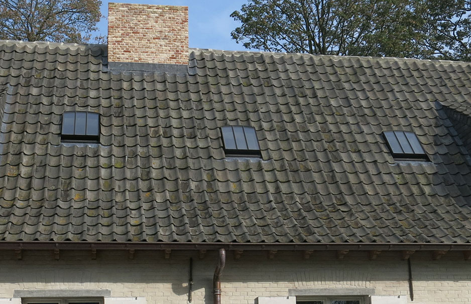 Dach mit traditionellen Ziegeln und Dachfenstern auf einem Wohnhaus Schräges Hausdach mit alten, moosbewachsenen Dachziegeln, drei modernen Dachfenstern und gemauertem Schornstein