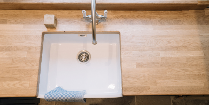 Moderne Spülbeckenlösung mit Holzarbeitsplatte und klassischer Armatur Küchenspüle in weiß mit Armatur auf heller Holzarbeitsplatte und einem blauen Geschirrtuch am Beckenrand