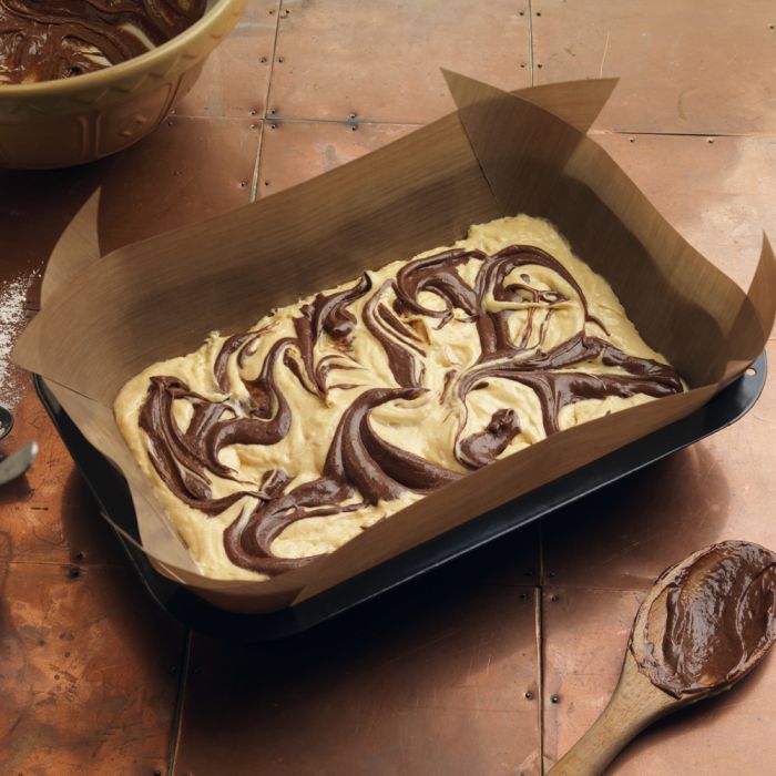 Ungebackener Marmorkuchen- oder Brownie-Teig mit Schokoladenswirls in einer rechteckigen Backform auf einer Kupferplatte