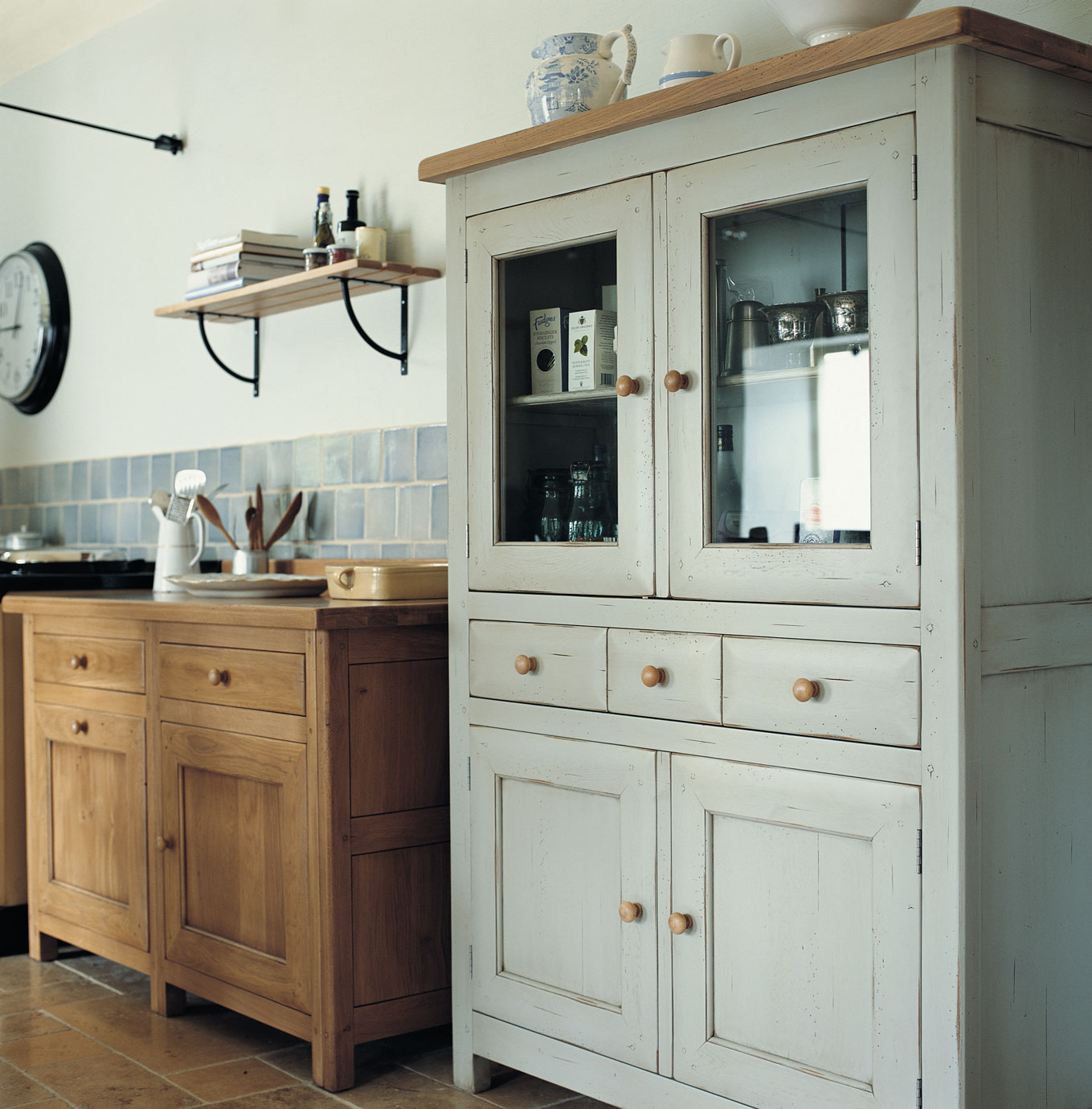 Landhausstil Küchenschrank aus Holz mit Glastüren und klassischer Küchenzeile Küchenschrank im Landhausstil aus Holz mit Glastüren, neben einer rustikalen Küchenzeile in einer gemütlichen Küche mit hellen Fliesen und Dekoration.